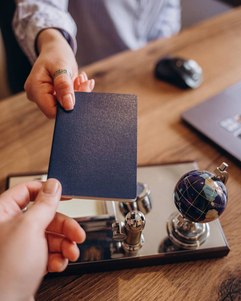 A passport handed across a desk beside an official stamp and a small globe