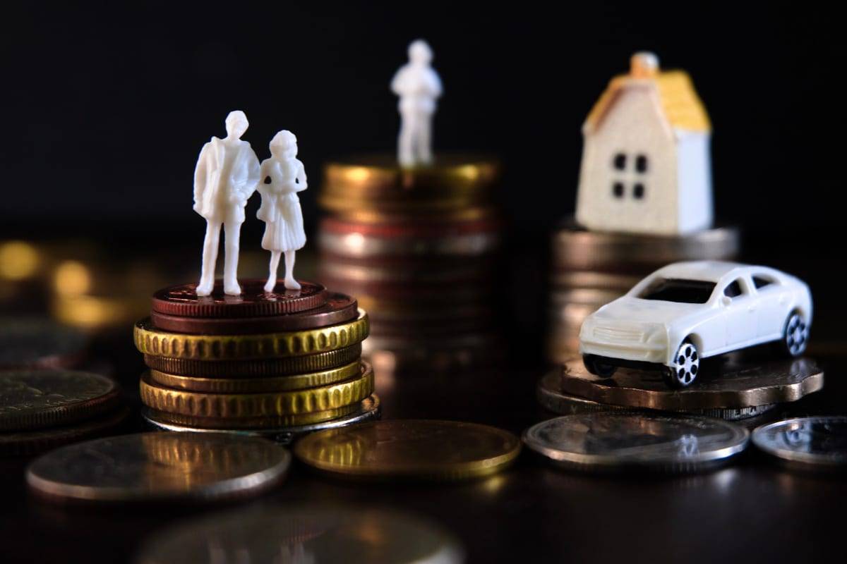 Miniature figures of a couple, a house and a car standing on stacks of coins