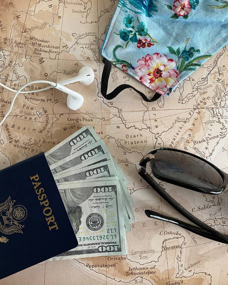 A passport with US dollar notes, sunglasses and earphones laid out on a vintage world map