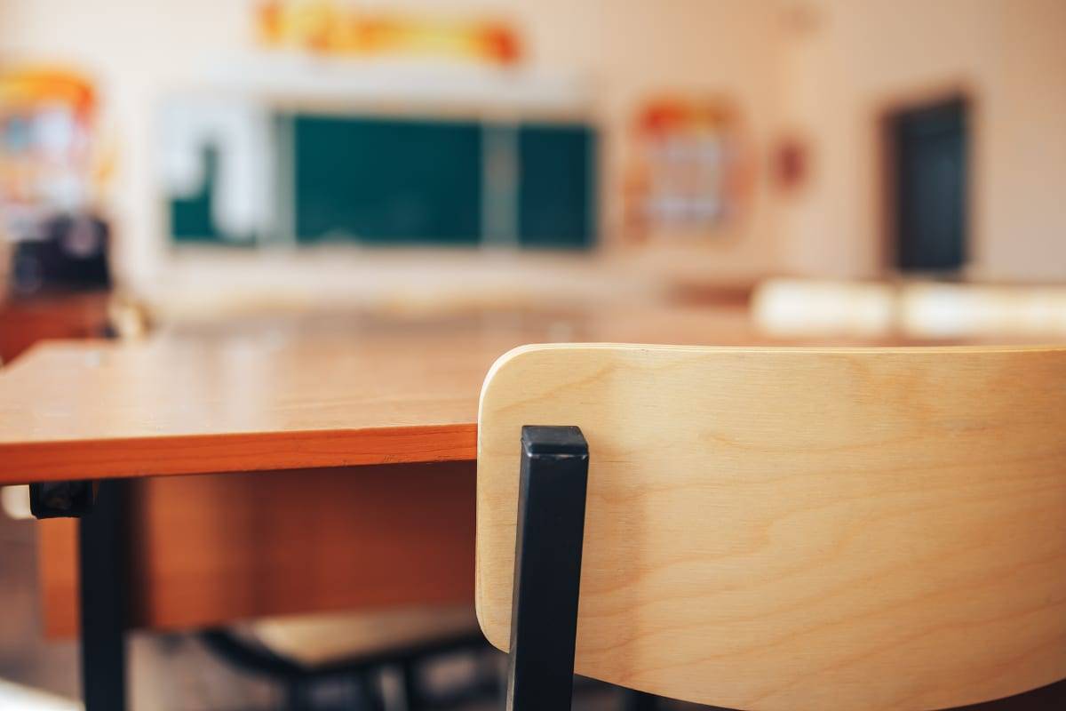 An empty wooden desk and chair in a bright primary-school classroom with a green chalkboard