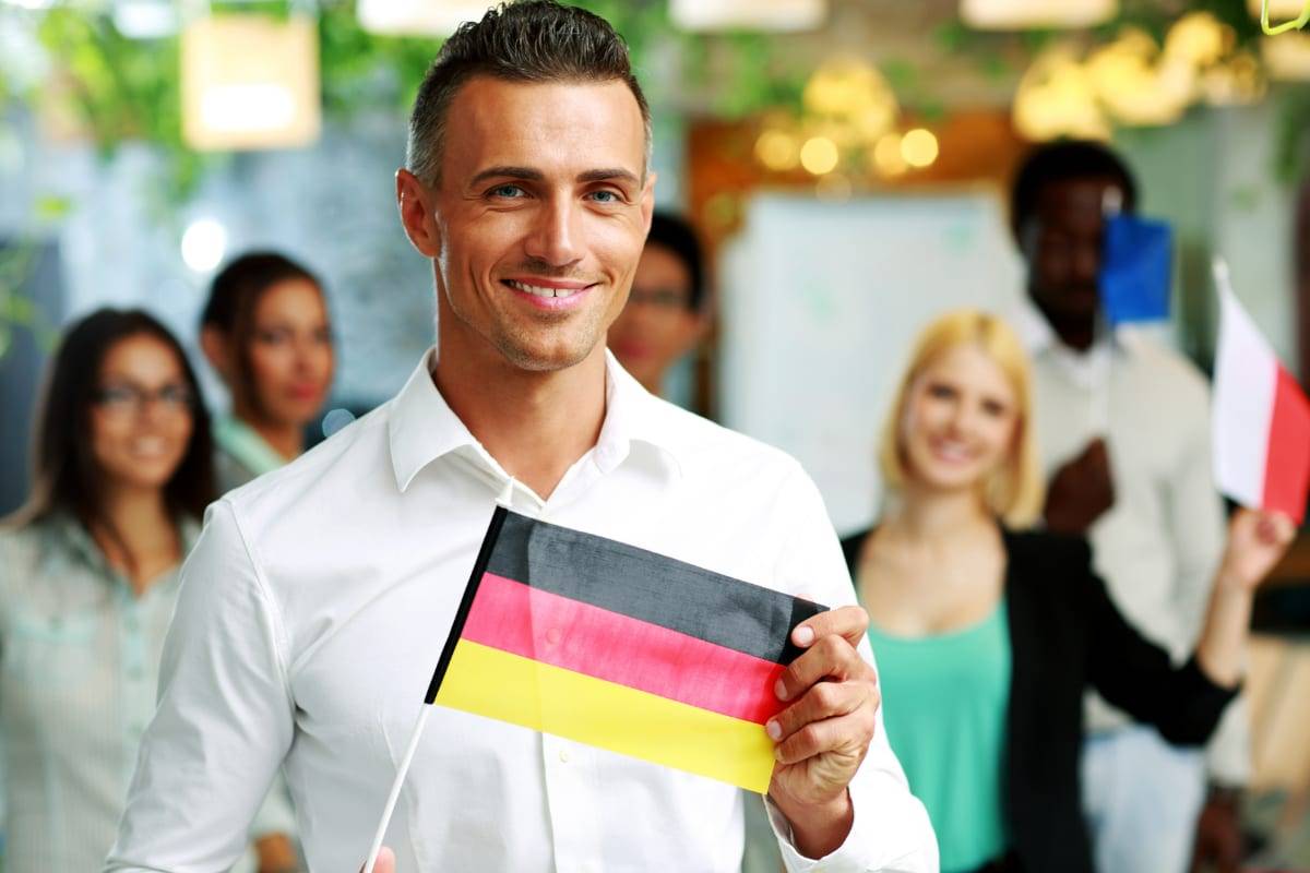 A businessman holding a small German flag in front of a smiling office team