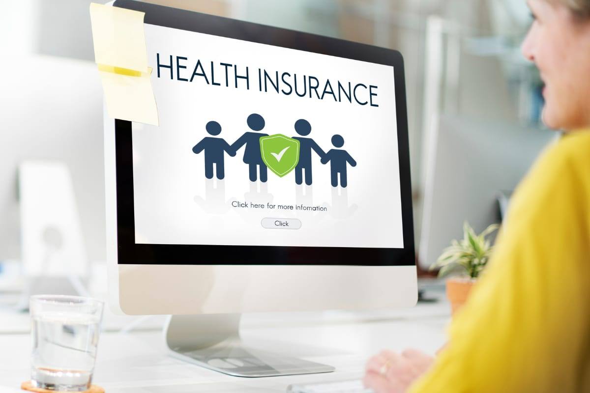 A desktop screen showing a HEALTH INSURANCE graphic with a family and a green shield, viewed over a woman's shoulder