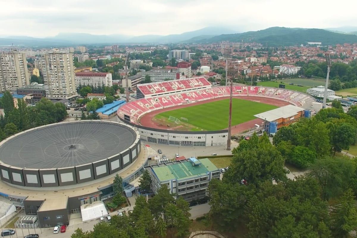 Aerial view of the Čair stadium and round sports hall in Niš, with the city and hills behind.