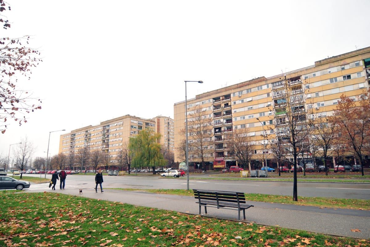 Long apartment blocks beside a park scattered with autumn leaves in the Novo Naselje district of Novi Sad.