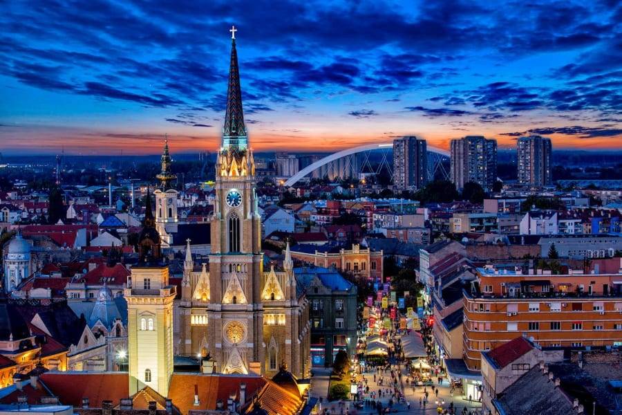 The lit spire of the Name of Mary Church above the old town rooftops at twilight, Novi Sad, Serbia