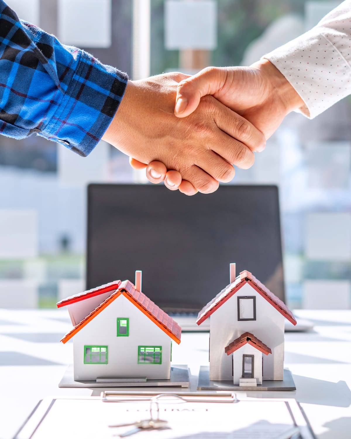 A handshake over two model houses, a set of keys and a property contract