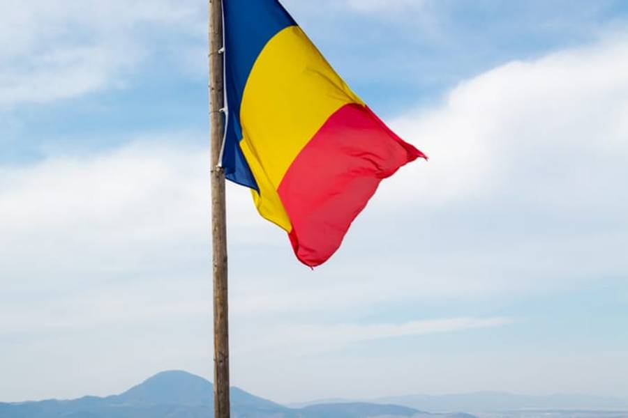 The Romanian national flag flying on a hilltop above distant mountains, Romania