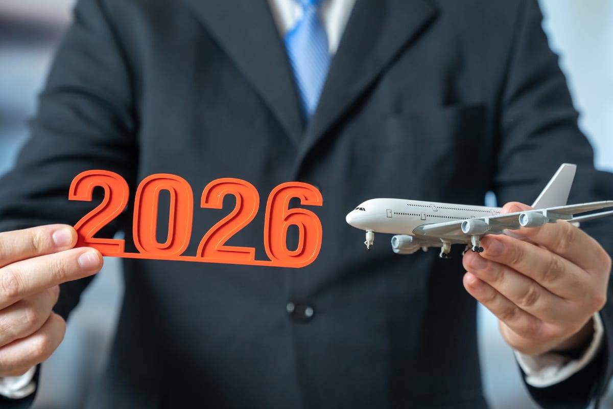 A person in a suit holding a 2026 sign in one hand and a model airplane in the other