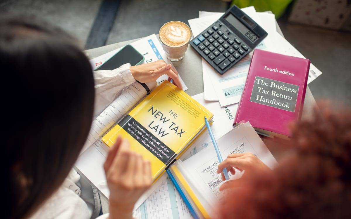 Two people reading tax law books beside a calculator, coffee and paperwork