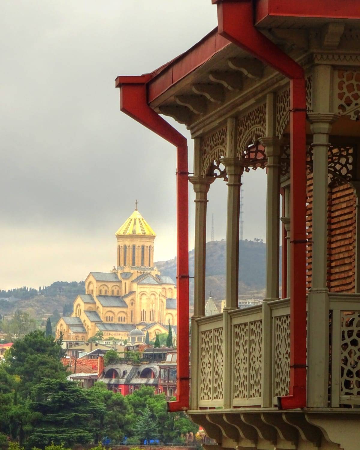 The golden dome of Tbilisi's Sameba Cathedral seen past a traditional carved balcony, Georgia