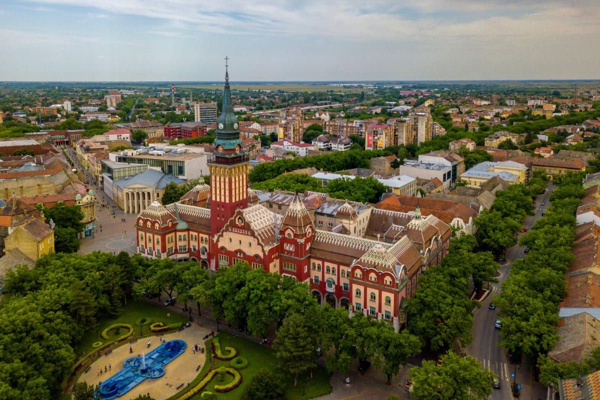 Flyfoto av jugendstilrådhuset i Subotica og fontenehagen, med byen som brer seg ut bak.