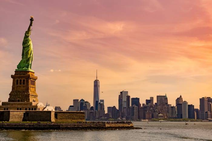 The Statue of Liberty at sunset with the Lower Manhattan skyline and One World Trade Center behind, New York, United States