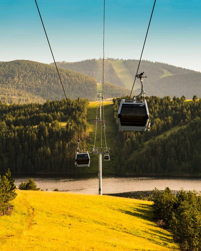 The Gold Gondola cabins gliding over green hills and a lake, Zlatibor, Serbia